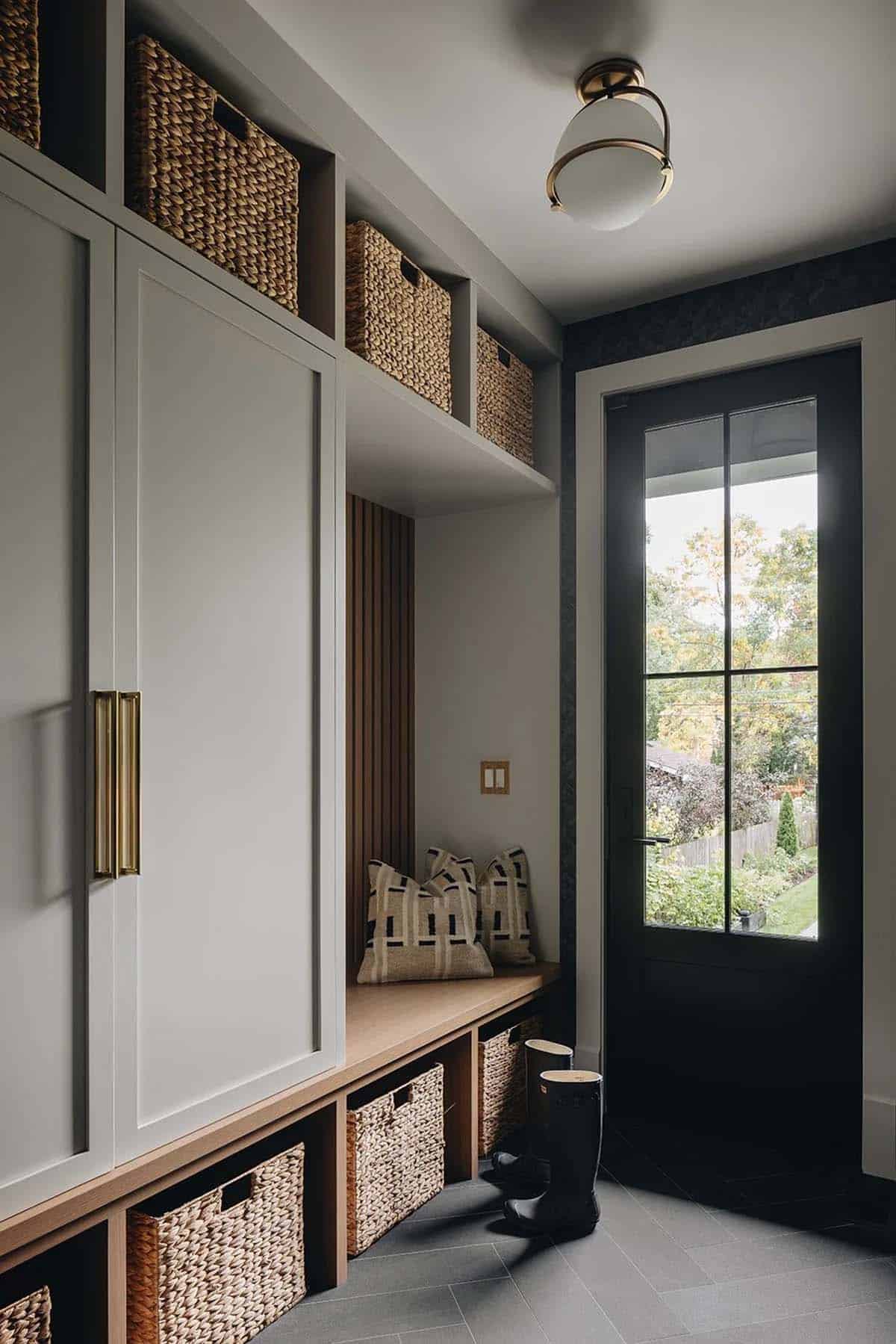 Mudroom with cream built-in cabinetry, woven basket storage, a wood bench seat, herringbone tile floor, and a glazed black back door
