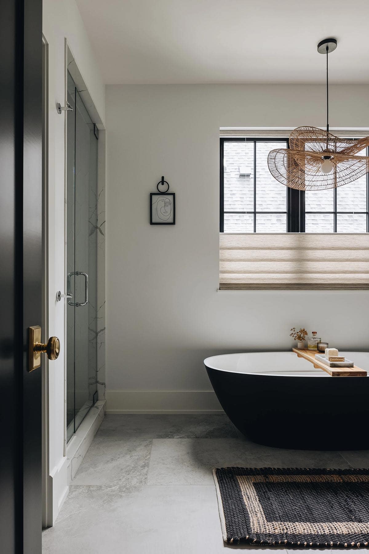 Primary bathroom with a matte black oval freestanding soaking tub, woven rattan pendant, gray stone tile floor, and a glass-enclosed marble shower