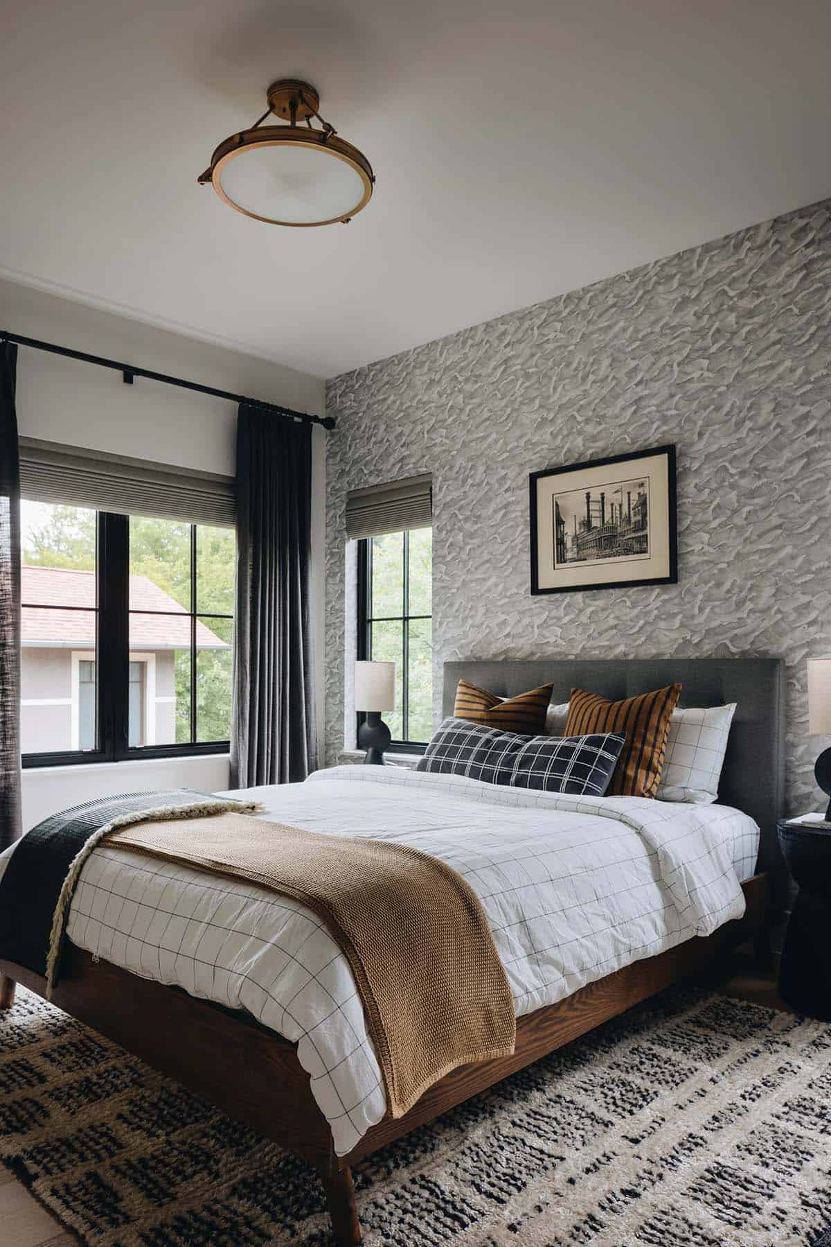 Boy's bedroom with a textured gray wallpaper accent wall, wood platform bed, plaid and striped throw pillows, dark velvet curtains, and a brass flush-mount ceiling light