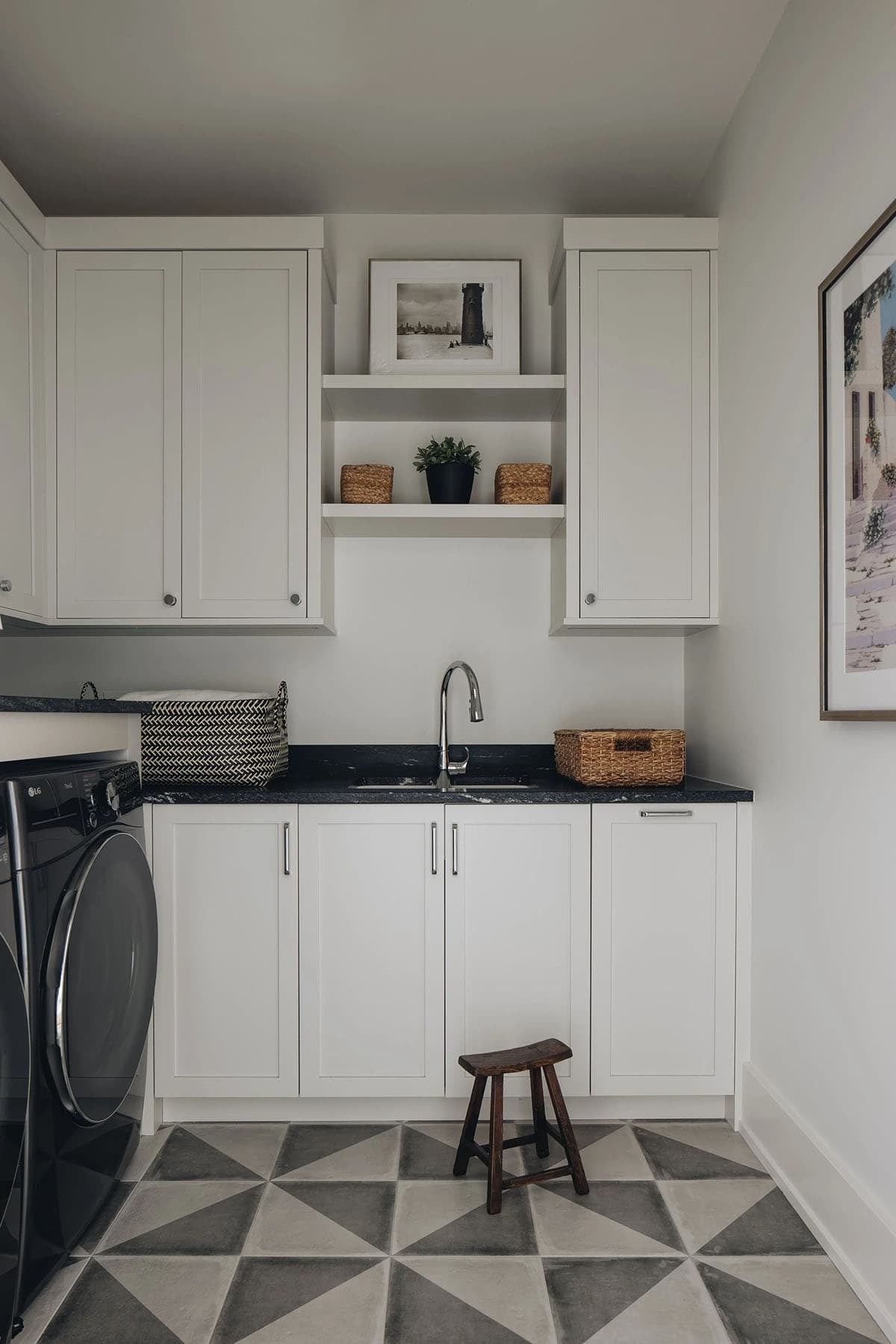 Laundry room with white shaker upper and lower cabinets, black granite countertop, built-in open shelving, geometric gray tile floor, and an LG front-load washer