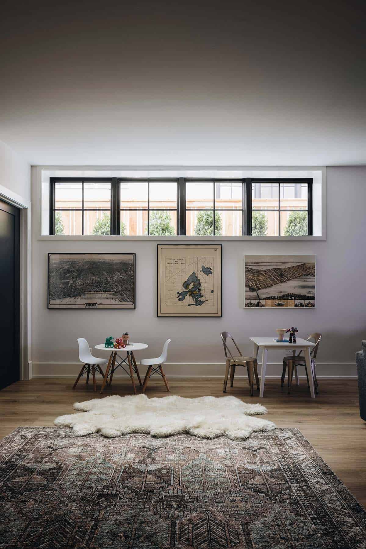 Children's playroom with a wide clerestory window, vintage map gallery wall, two small round play tables with molded chairs, a sheepskin rug, and an antique area rug