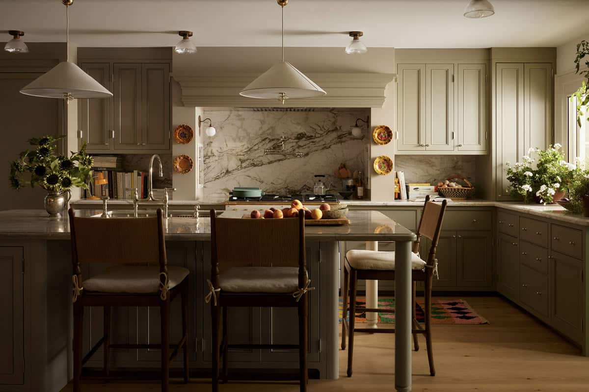 Sage green kitchen with marble backsplash and cane-back barstools at island