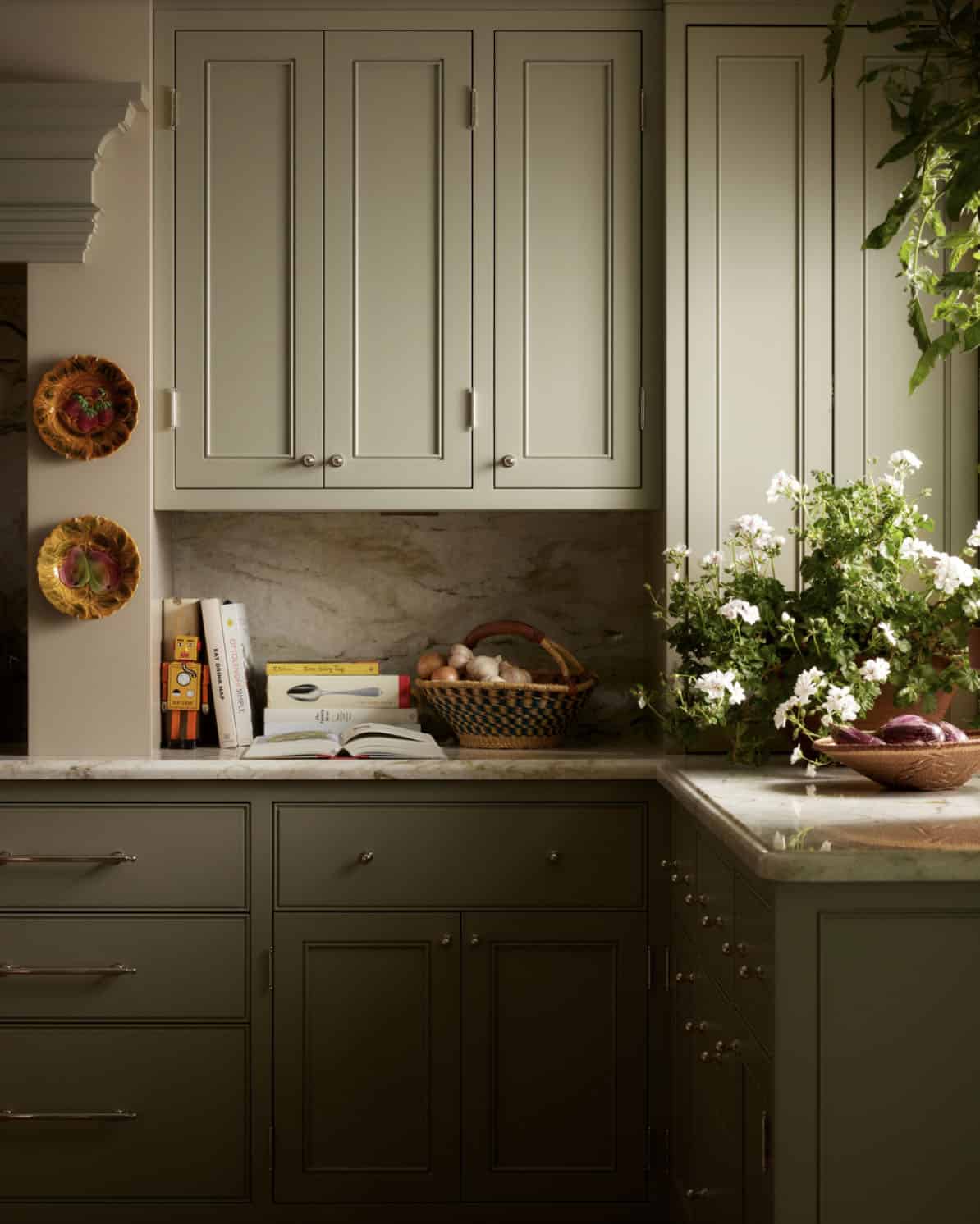 Close-up of olive cabinetry with countertop books, basket, and geraniums