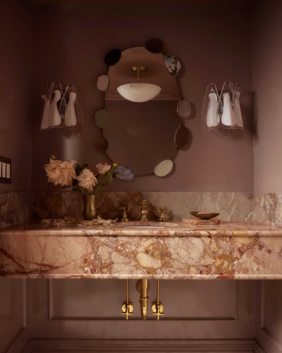 Pink marble powder room vanity with scalloped mirror and sconces