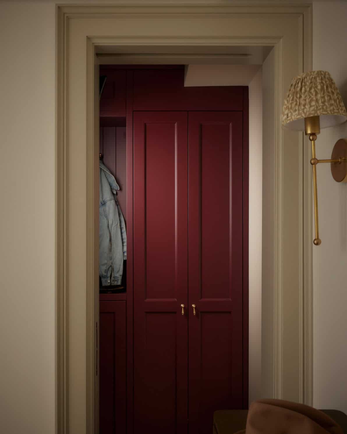 Burgundy paneled closet doors in cream hallway with brass sconce
