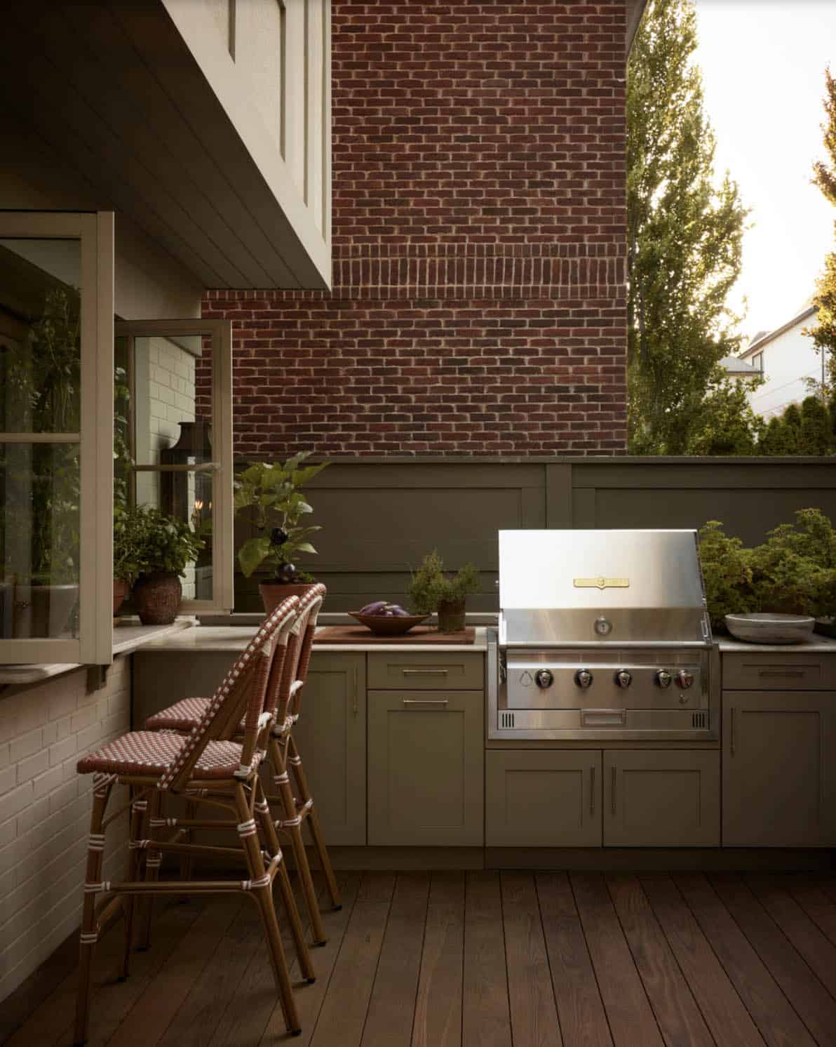 Outdoor kitchen with built-in grill against brick and olive cabinetry