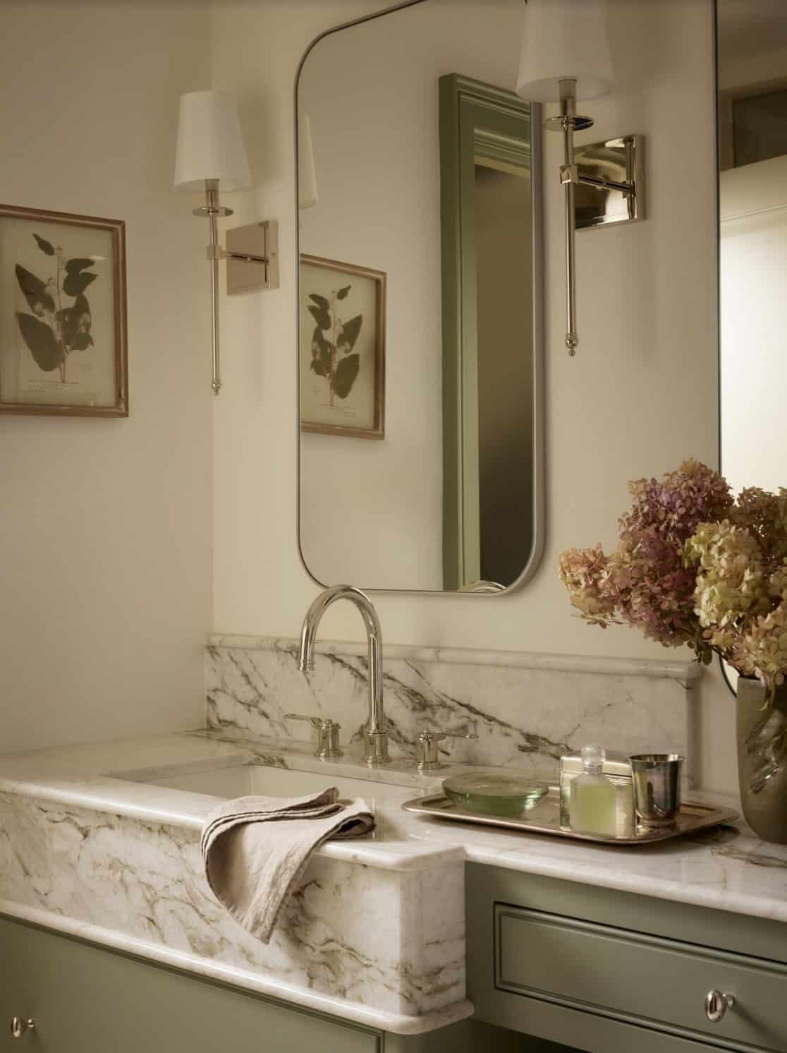 Close-up of marble vanity sink with botanical prints and sconces