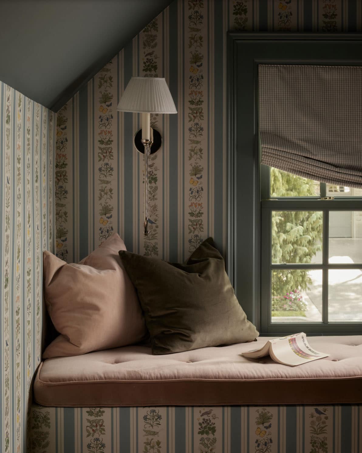Window seat corner with velvet pillows and floral striped wallpaper