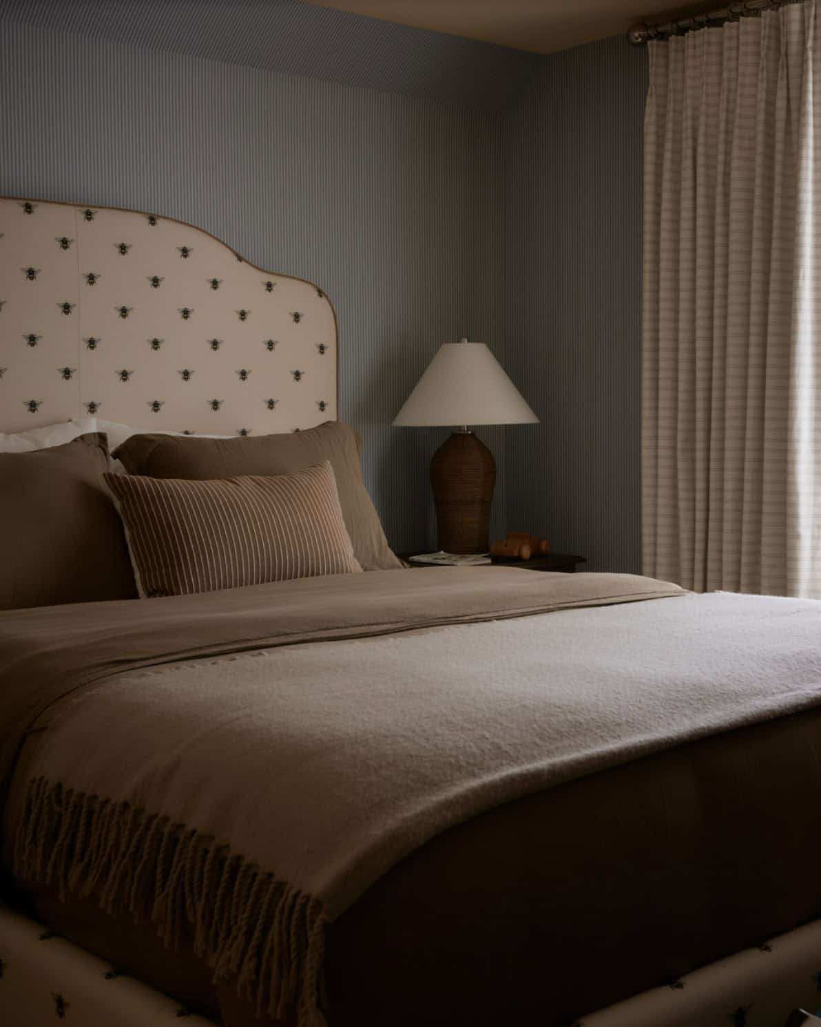 Bed with bee-print headboard and striped blue wallpaper