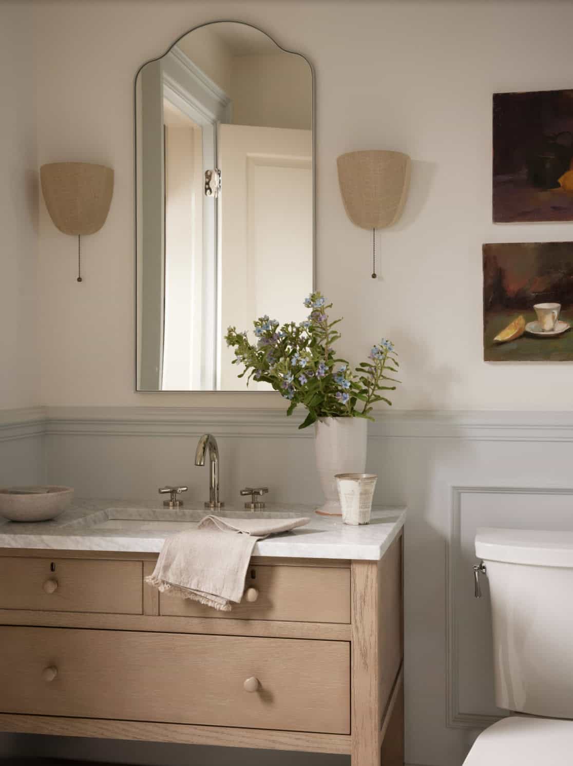 Bathroom vanity with arched mirror and still-life paintings