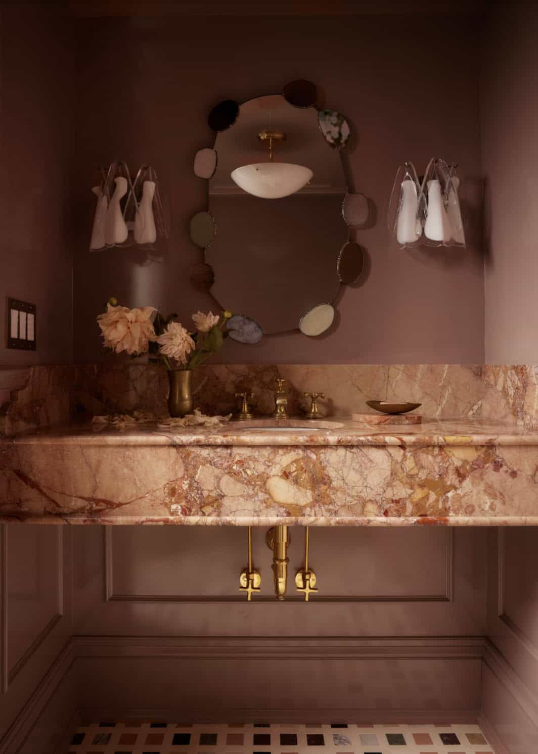 Pink marble powder room vanity with beaded oval mirror and brass fittings