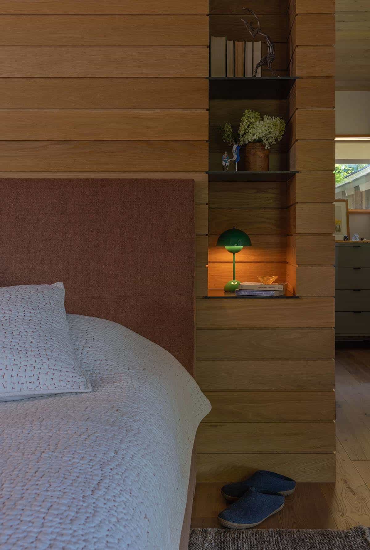 Bedroom detail showing horizontal oak plank wall with built-in open shelving and a glowing green mushroom lamp