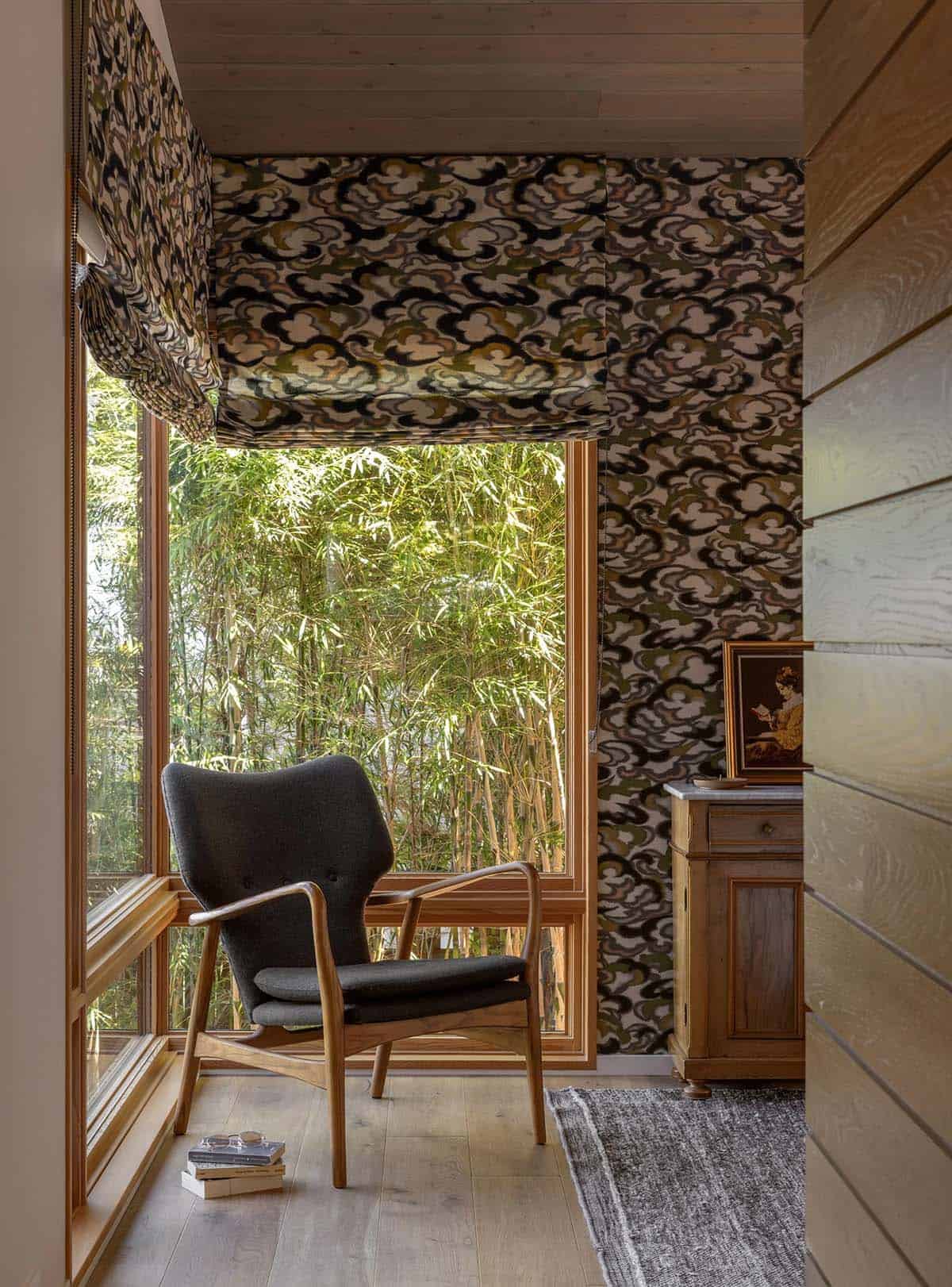 Bedroom reading nook with a Danish-style lounge chair set against bold cloud-patterned wallpaper and bamboo garden views