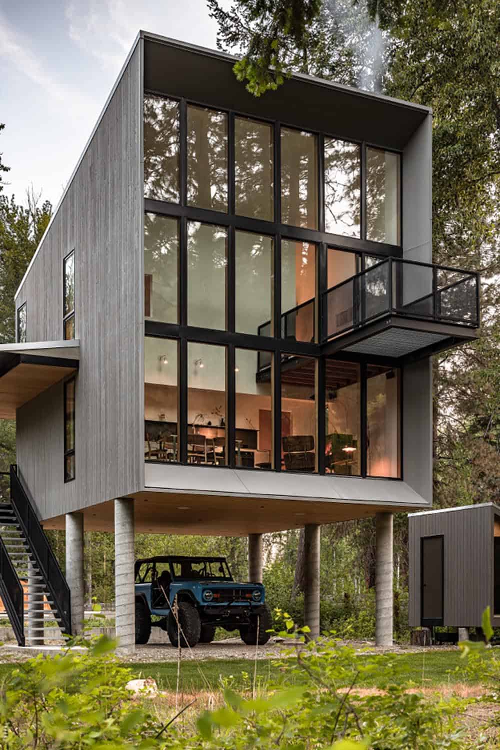 Modern cabin with full-height glass facade on concrete piers with vintage blue Jeep below