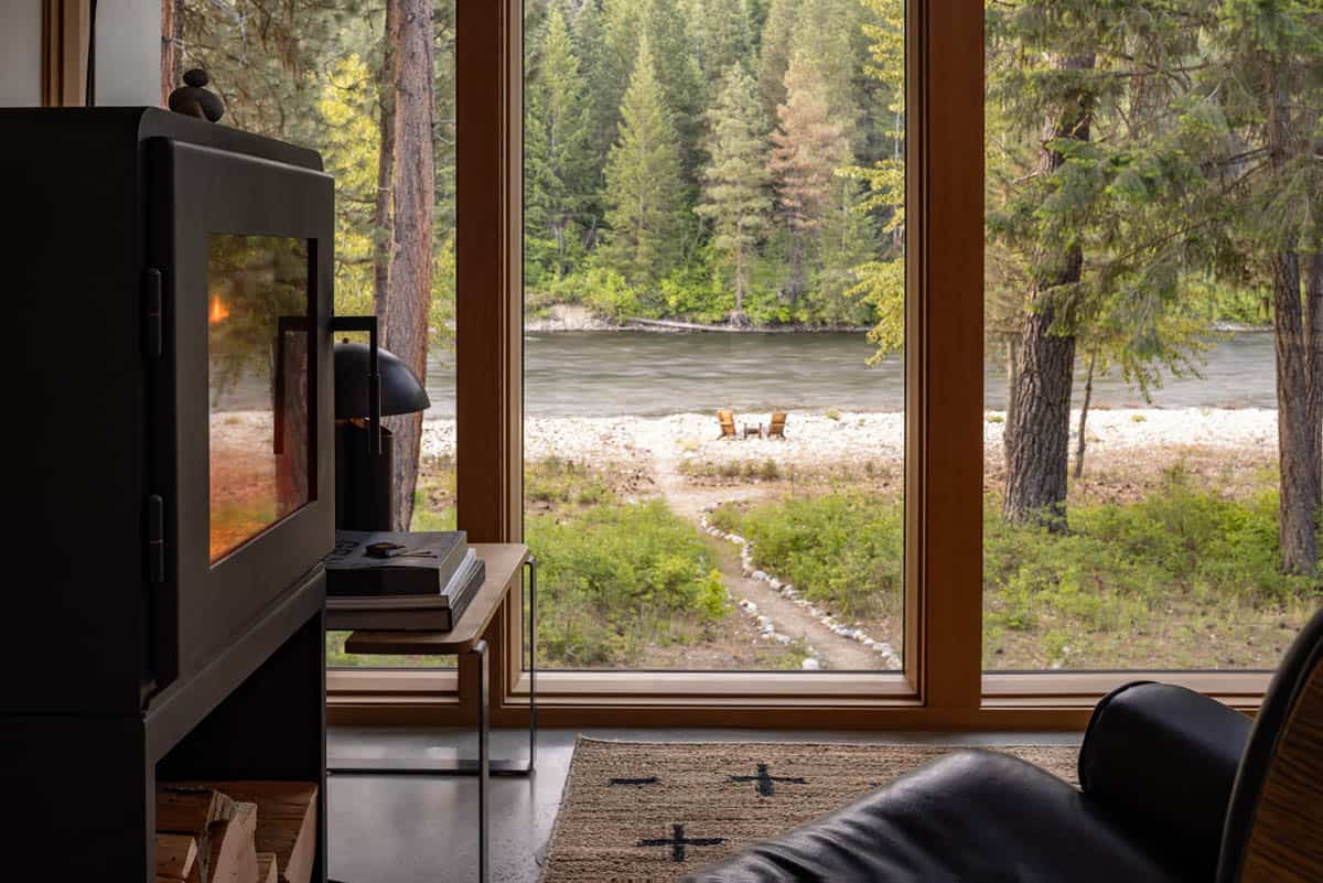 Interior view past wood stove through large windows to Wenatchee River and fire pit