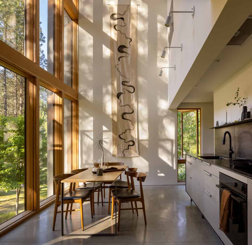 Dining area with double-height windows and textile wall art beside galley kitchen