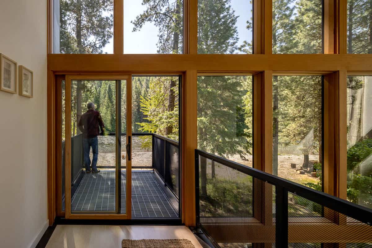 Man stepping onto elevated steel balcony through floor-to-ceiling wood-framed doors