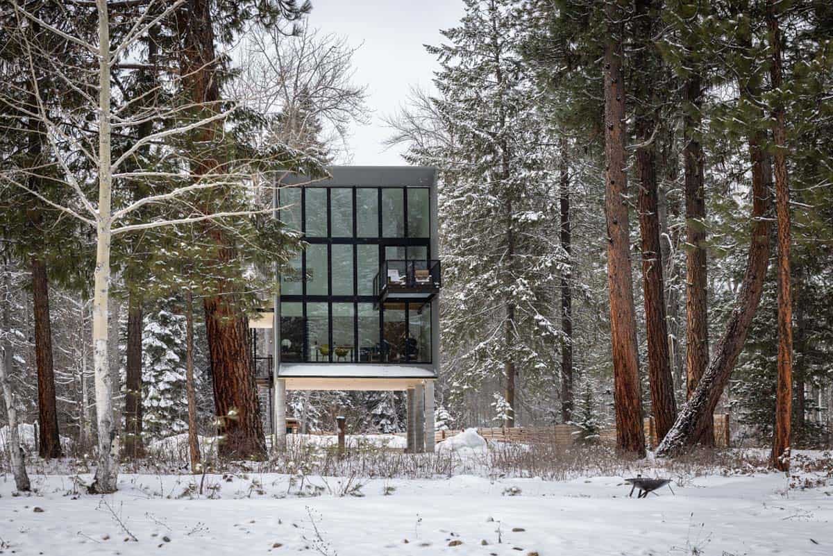 Modern glass cabin on stilts in snow-covered forest Washington winter