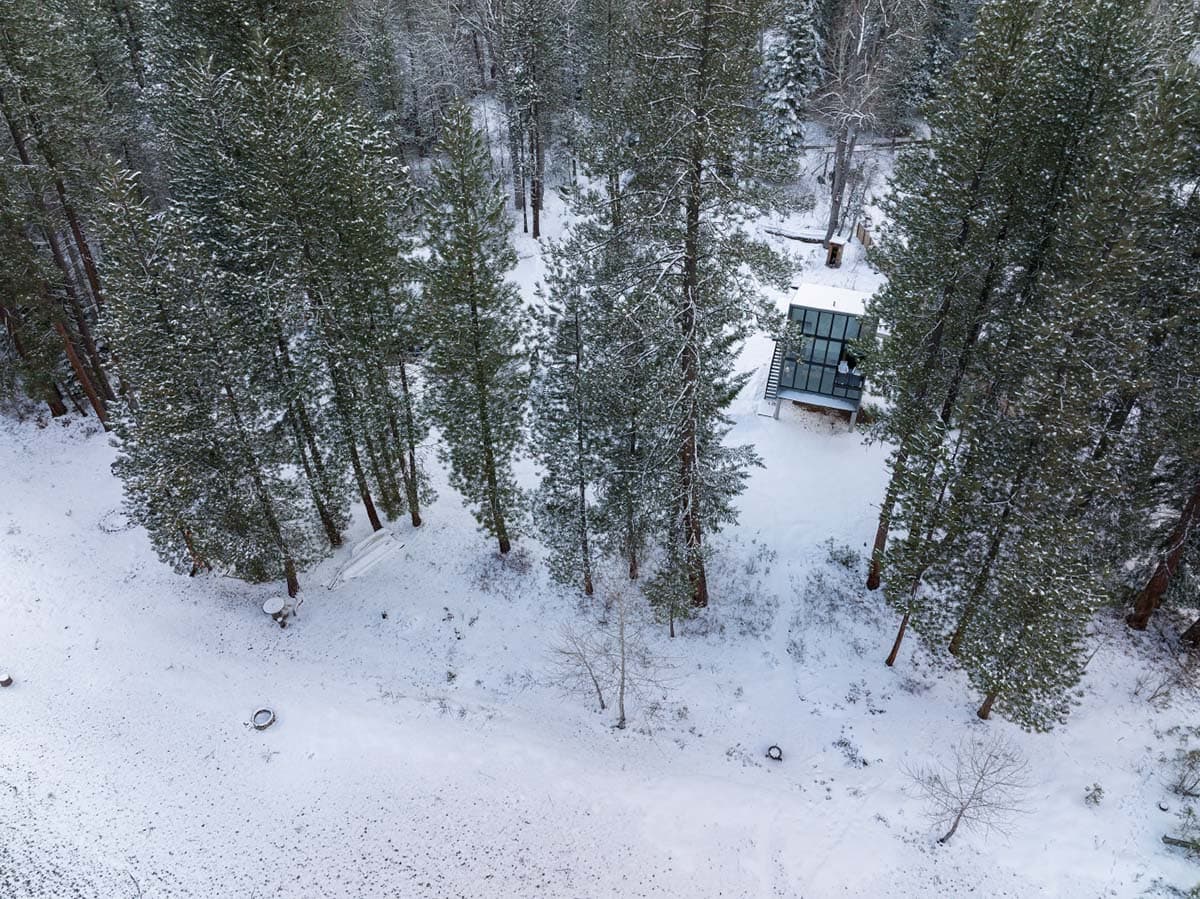 Aerial view of modern glass cabin nestled in snow-covered pine forest