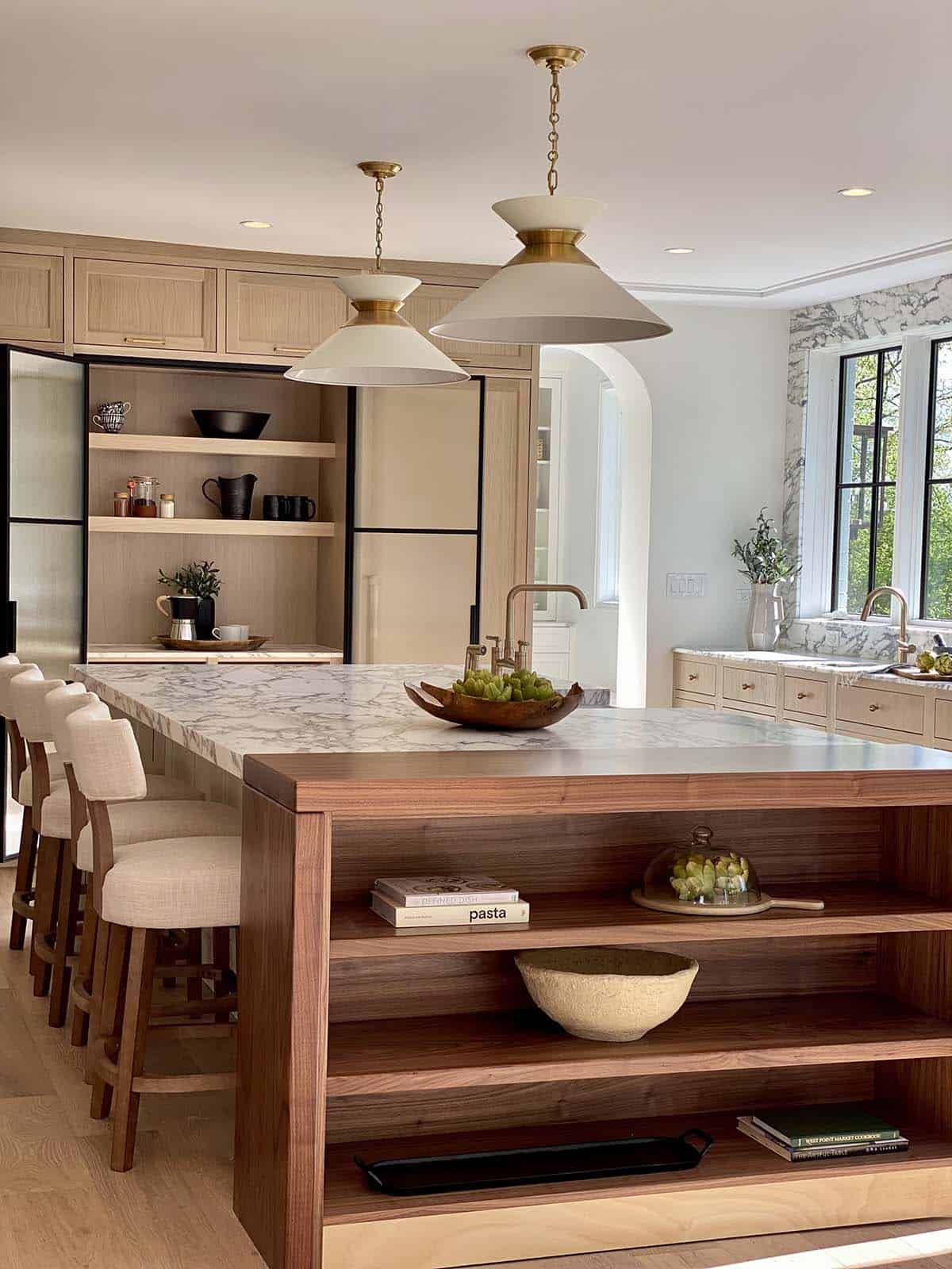 Kitchen island with walnut open shelving, marble waterfall countertop, and brass dome pendant lights over a breakfast bar