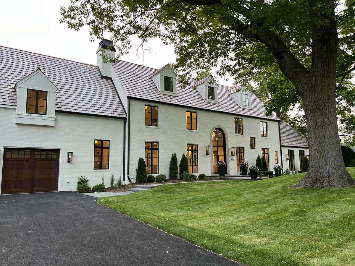 Exterior view of white brick manor home with arched front entry, black-framed windows, and cedar shake roof
