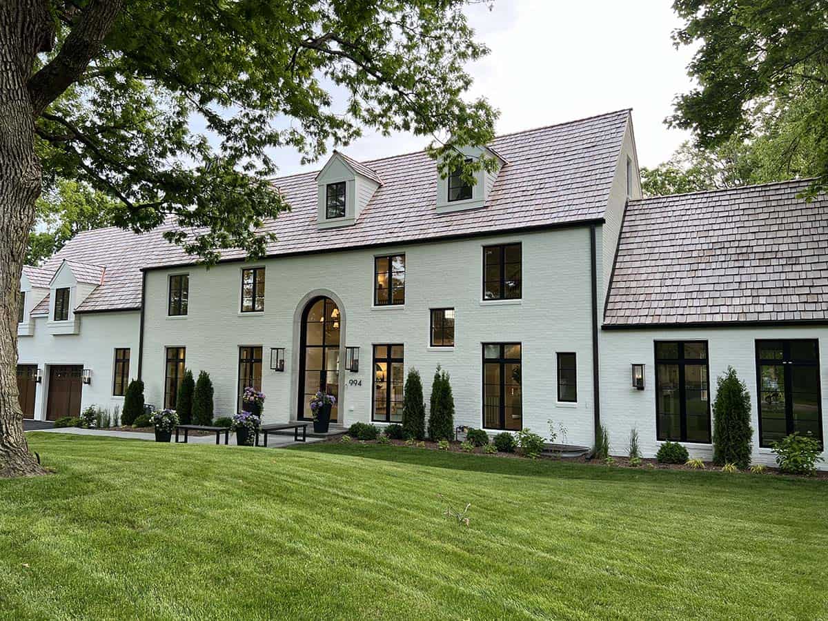 Front facade of white brick estate home with arched glass entry door and multiple gabled dormers
