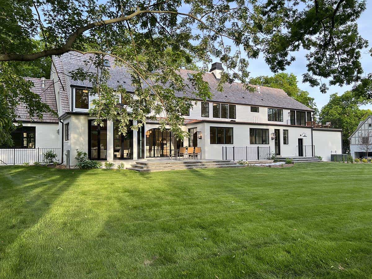 Rear exterior of white manor home with covered patio, outdoor dining area, and expansive lawn at sunset