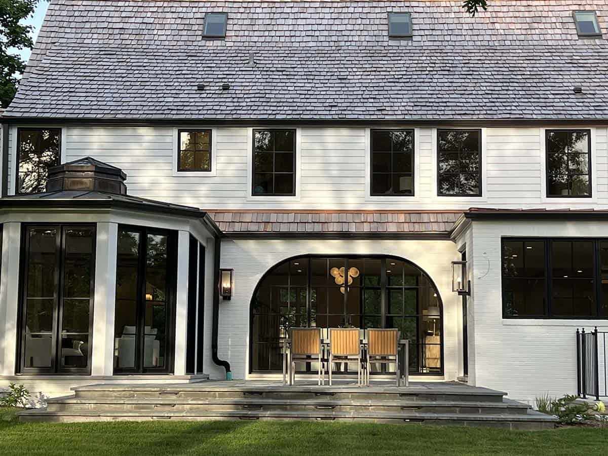 Rear patio with arched glass doors, copper roof accents, and outdoor dining table under a covered porch