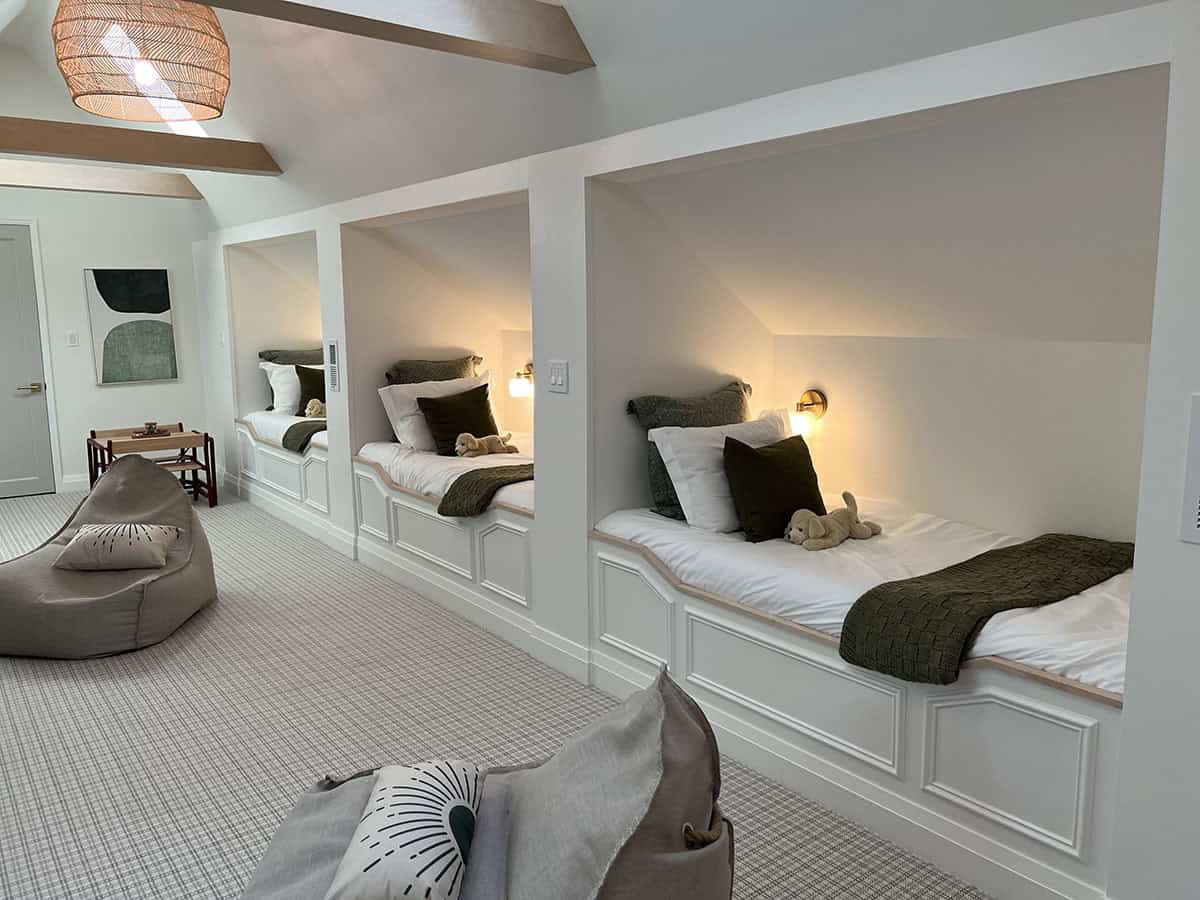 Built-in bunk nook bedroom with three white paneled beds, green throws, and a woven pendant light