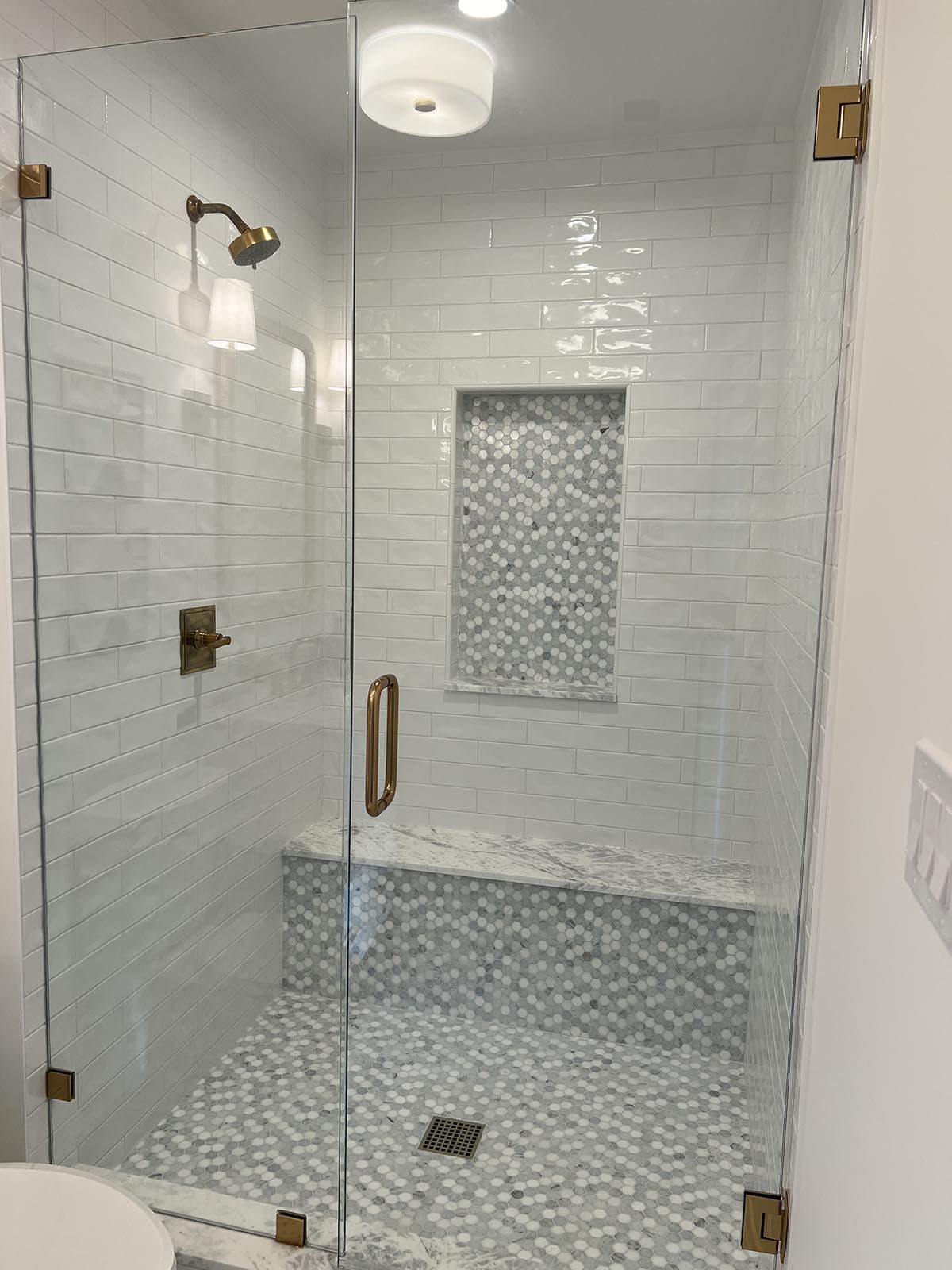 Frameless glass shower with white subway tile, hexagon mosaic accent niche, marble bench, and brass fixtures
