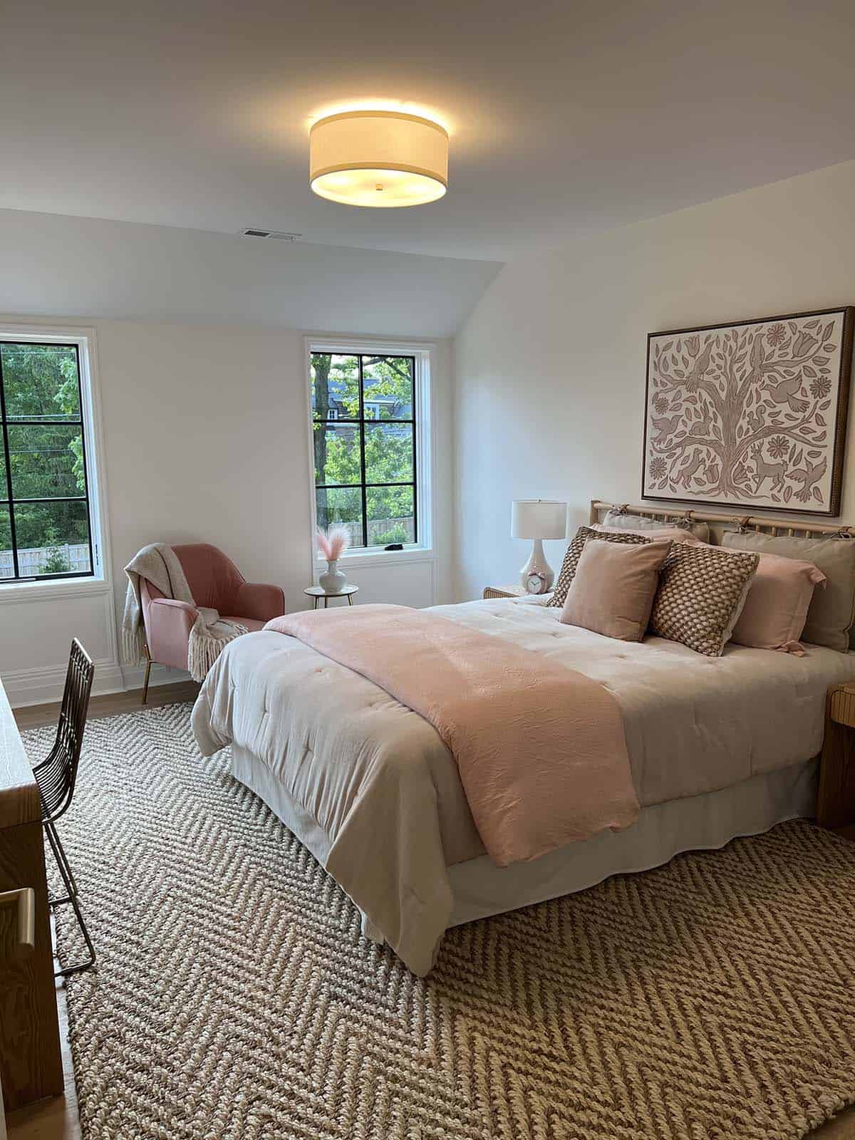 Cozy bedroom with blush pink bedding, pink accent chair, drum pendant light, and herringbone jute rug