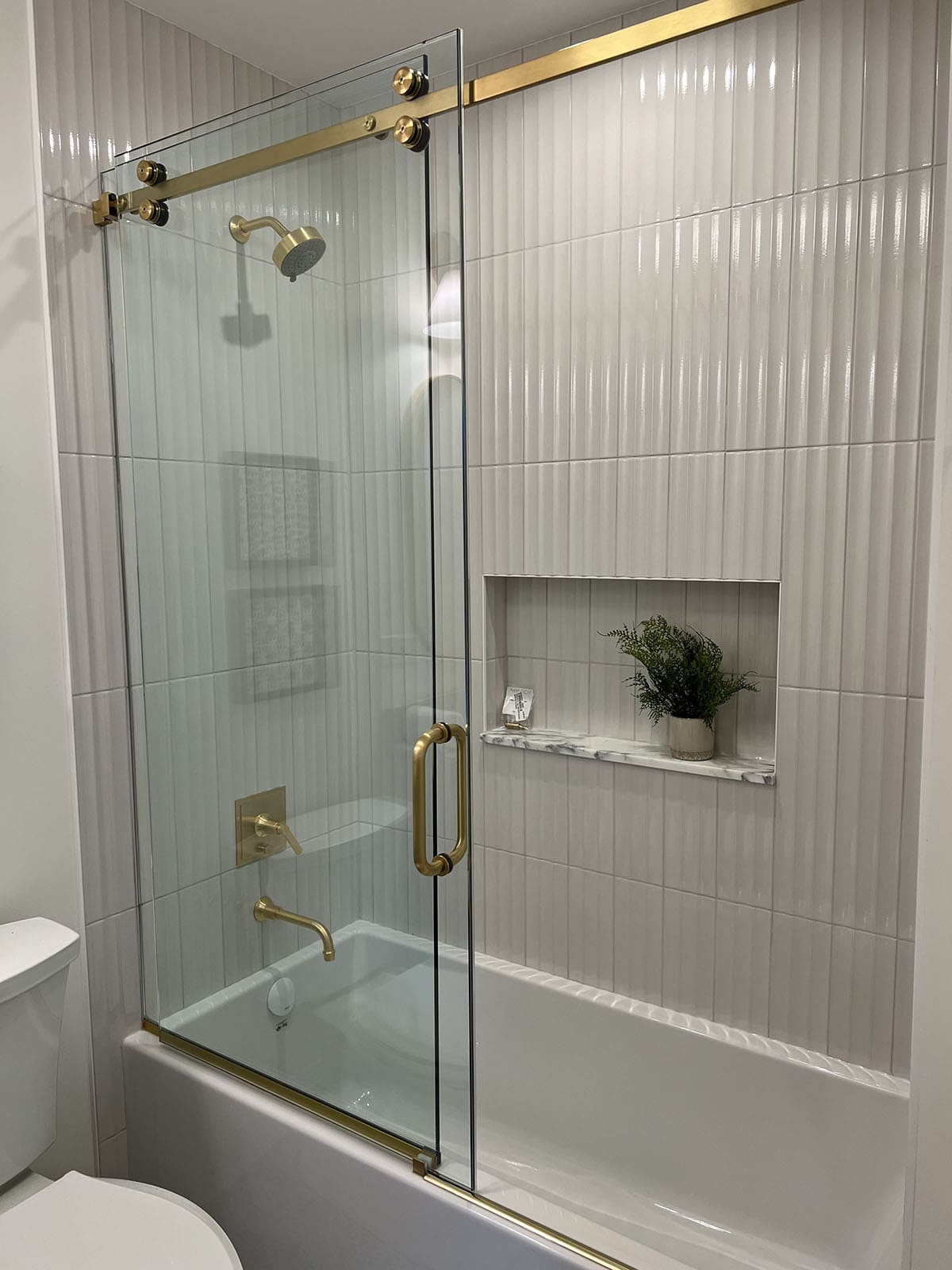 Tub-shower combo with vertical fluted tile, brass sliding glass door, and marble niche shelf