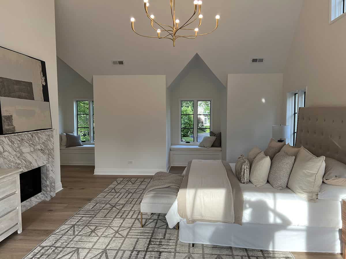 Primary bedroom with vaulted ceiling, gold chandelier, marble fireplace, and dual dormer window seats