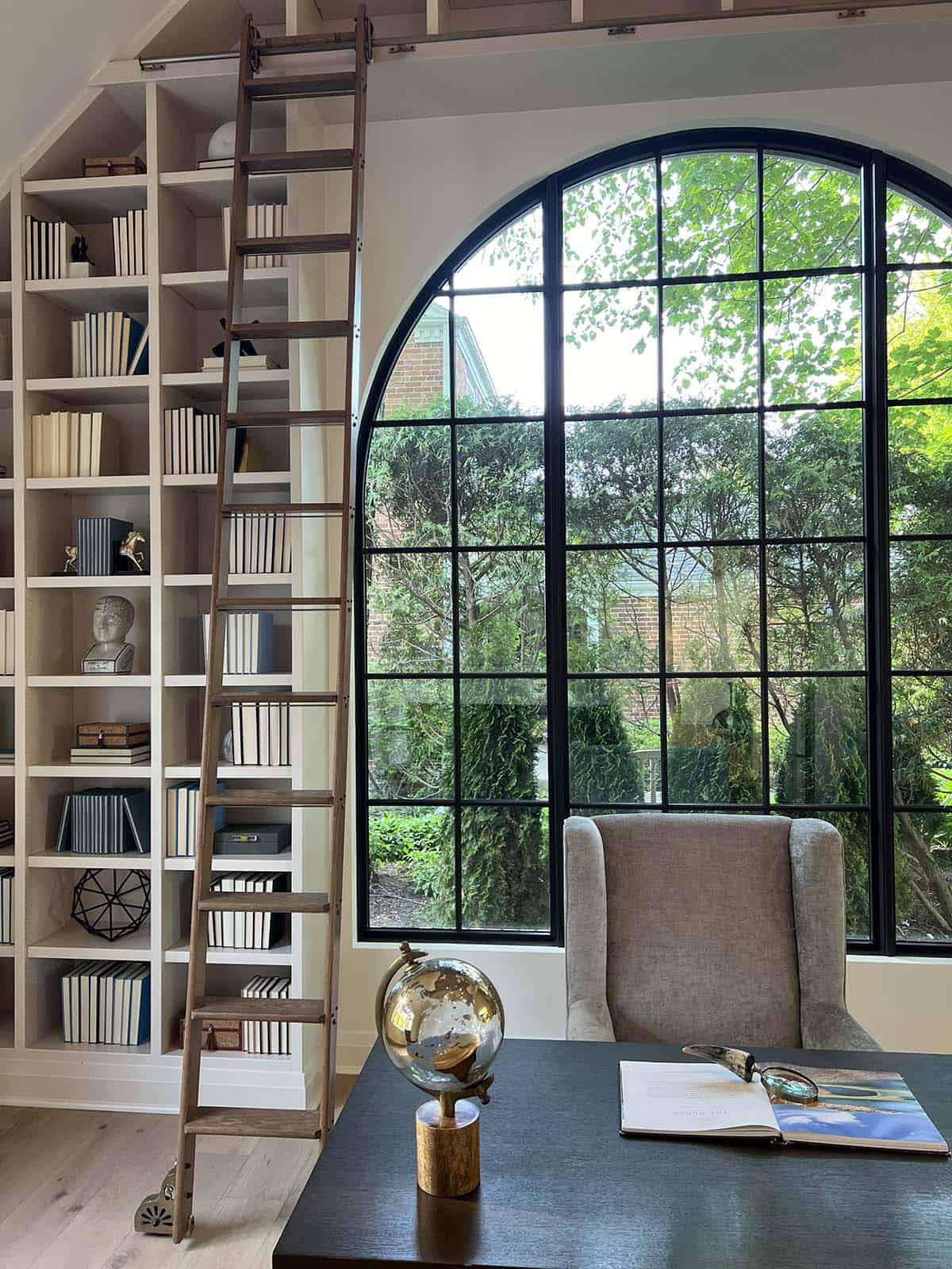 Home office library with floor-to-ceiling bookshelves, rolling ladder, and oversized arched steel window