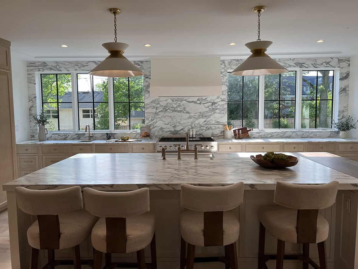 Kitchen with marble slab backsplash, brass pendant lights, and island seating with leather-trimmed stools