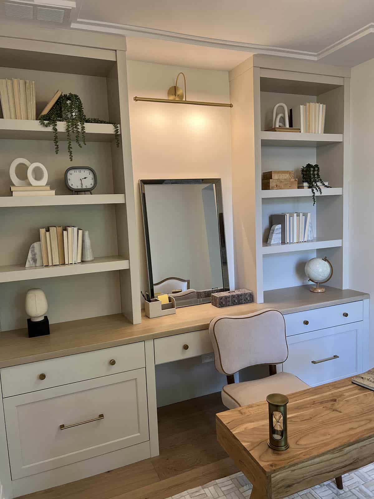 Built-in home office nook with open shelving, lighted vanity mirror, and desk with brass sconce