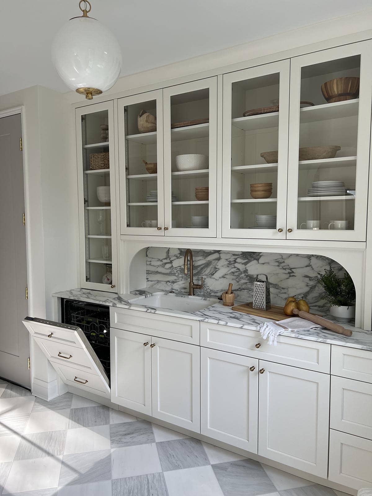 Butler's pantry with glass cabinetry, marble counters, built-in dishwasher, and checkered marble floor