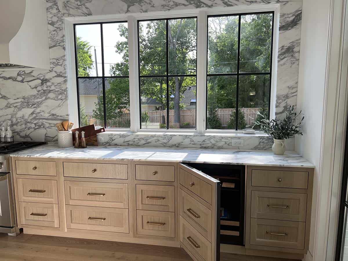 Kitchen counter with wine fridge, marble backsplash, oak cabinetry, and steel-framed window