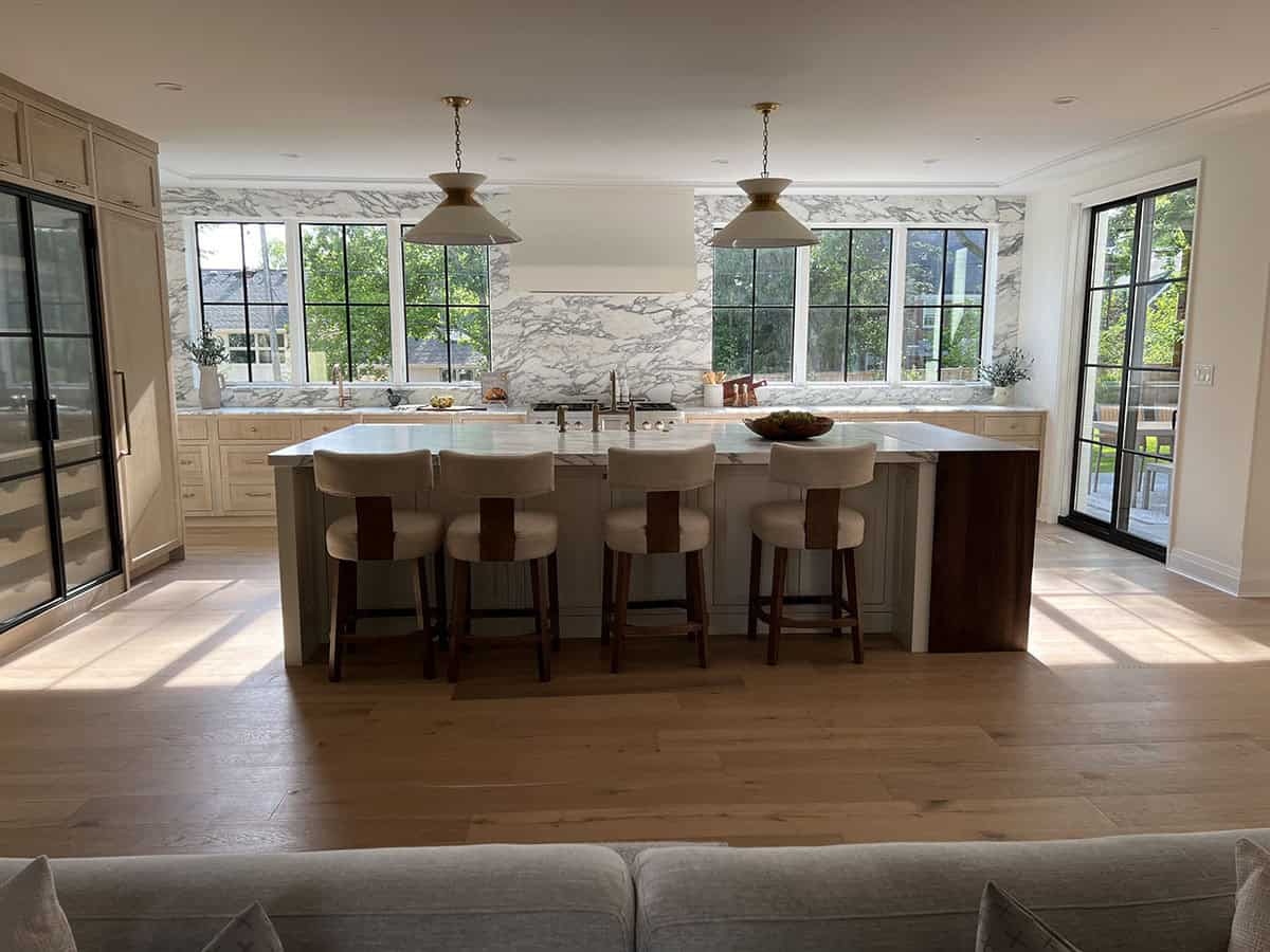 Open-concept kitchen island with counter stools, brass pendant lights, and marble backsplash wall