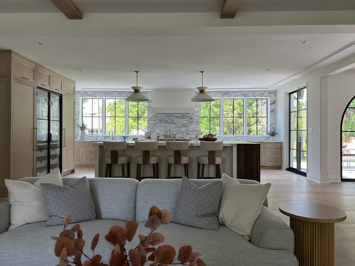Living room view toward kitchen island with beamed ceiling, gray sectional, and marble backsplash