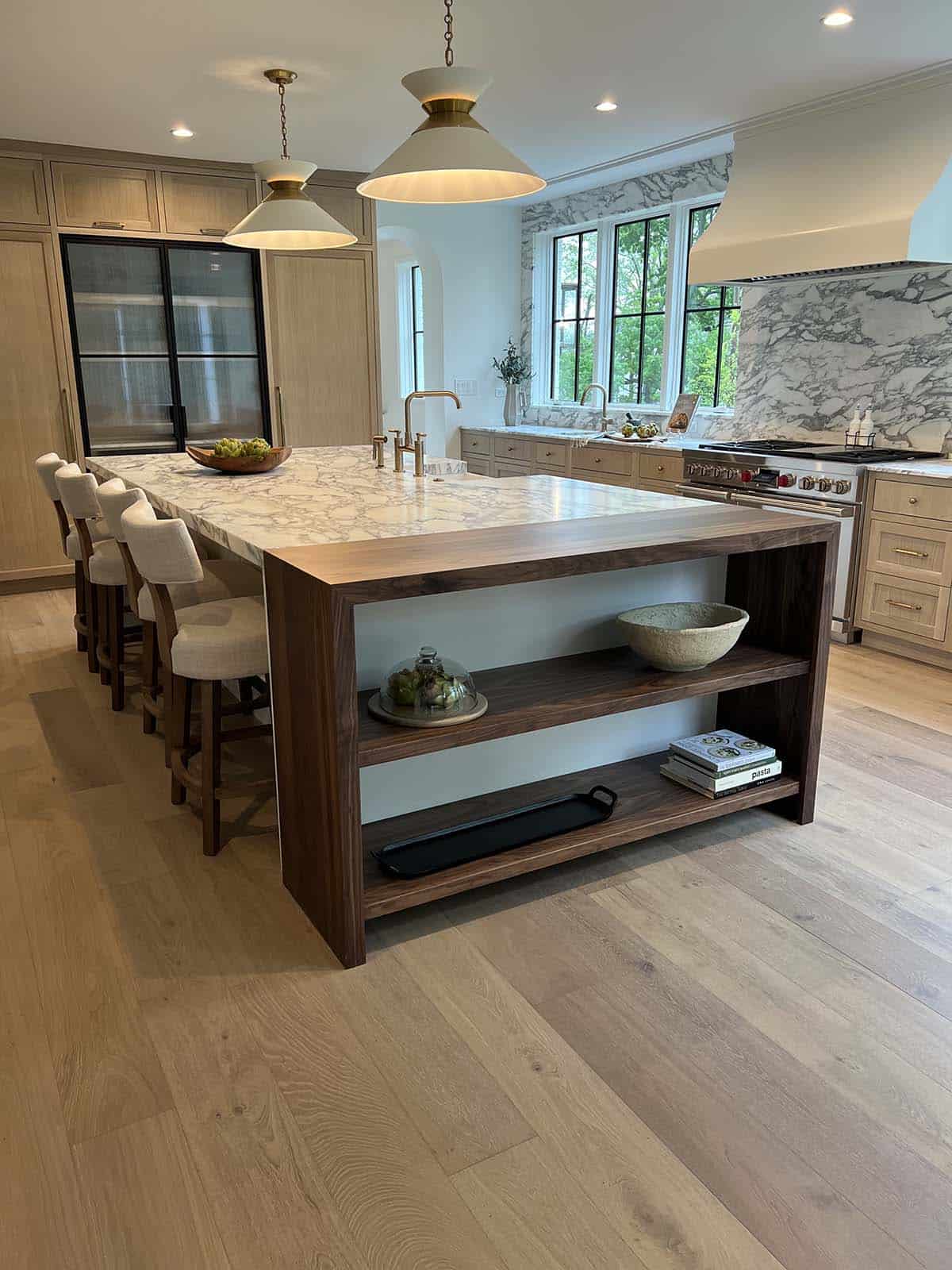 Walnut kitchen island with open shelving, marble waterfall countertop, and brass pendant lighting