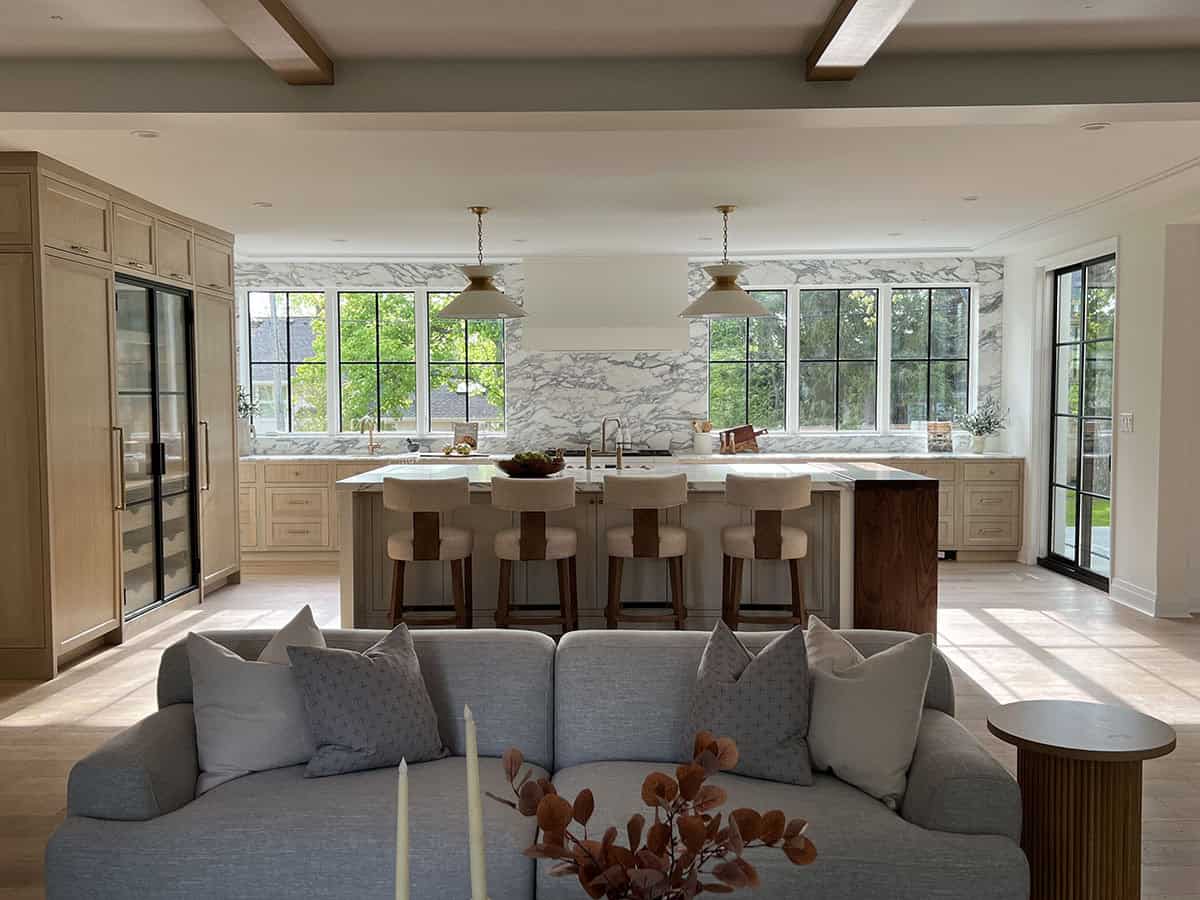 Great room with beamed ceiling, gray sofa, kitchen island, and arched glass doorway beyond