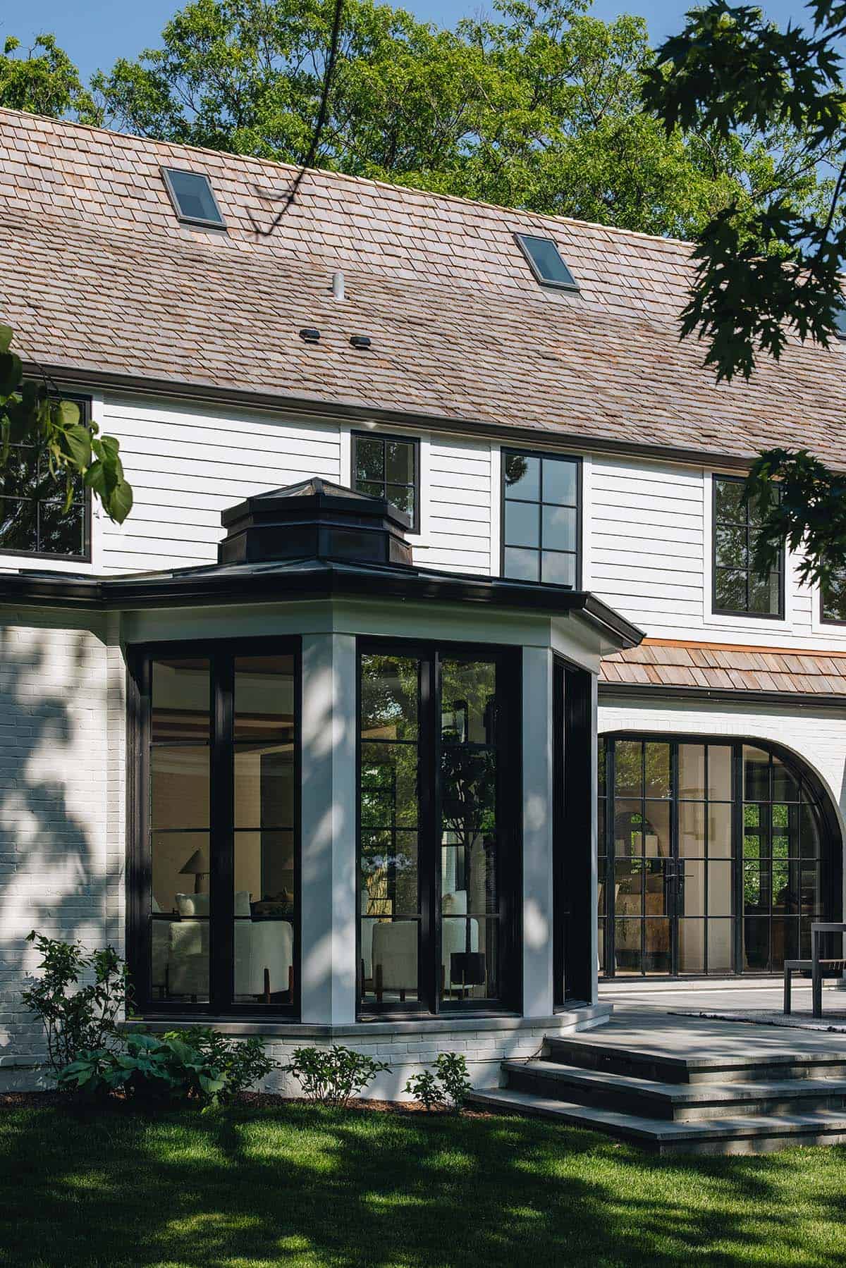 Exterior sunroom bump-out with black-framed windows, copper cupola roof, and cedar shake siding