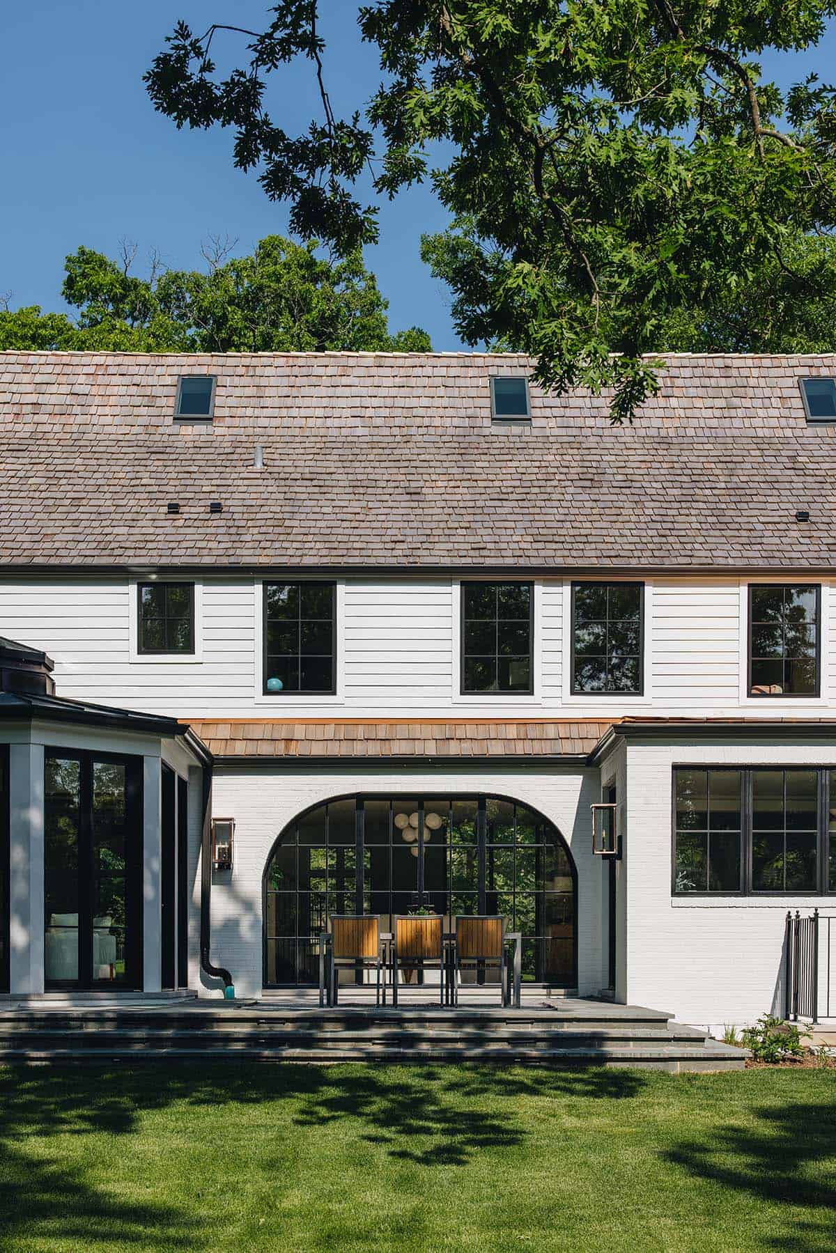 Rear facade with arched glass dining porch, cedar shake roof, and white shiplap siding