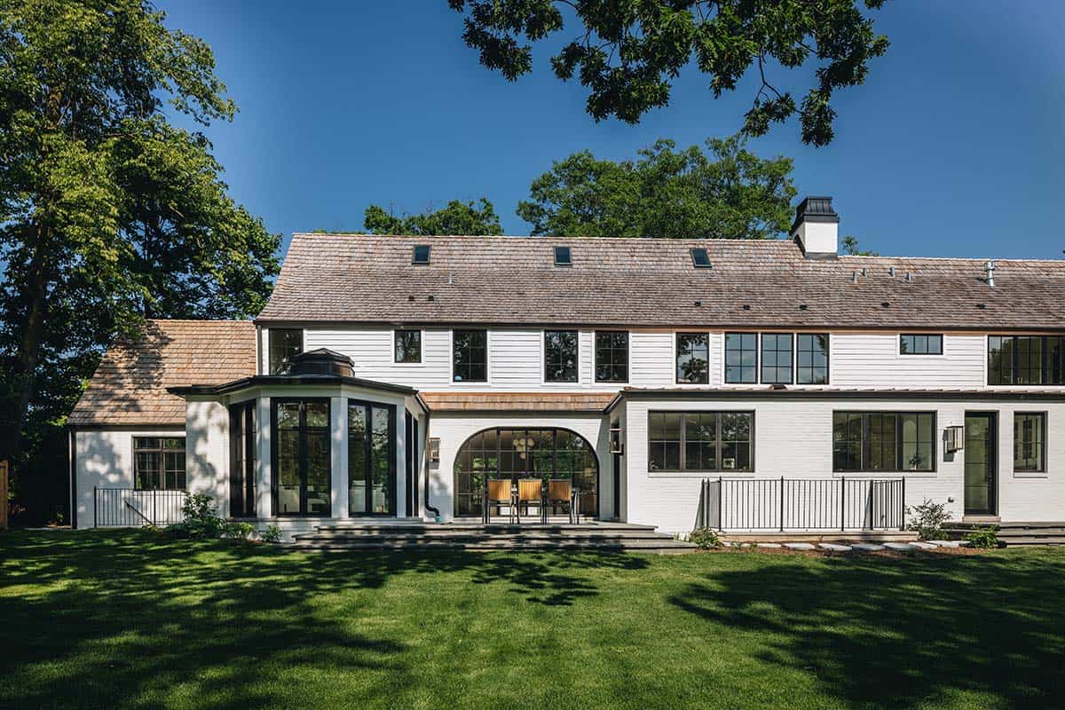 Rear exterior view of white shingle-style home with arched porch and copper-roofed sunroom