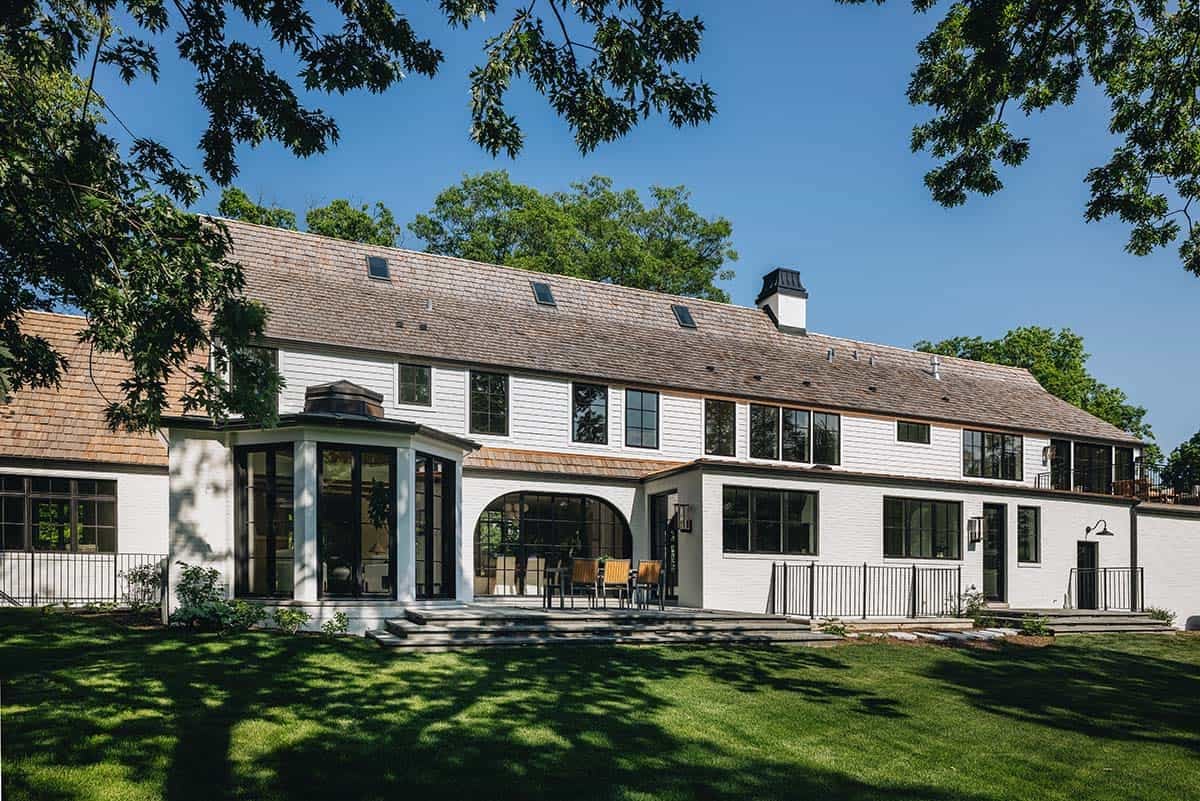 Angled rear view of white manor home with arched dining porch and multiple black-framed windows