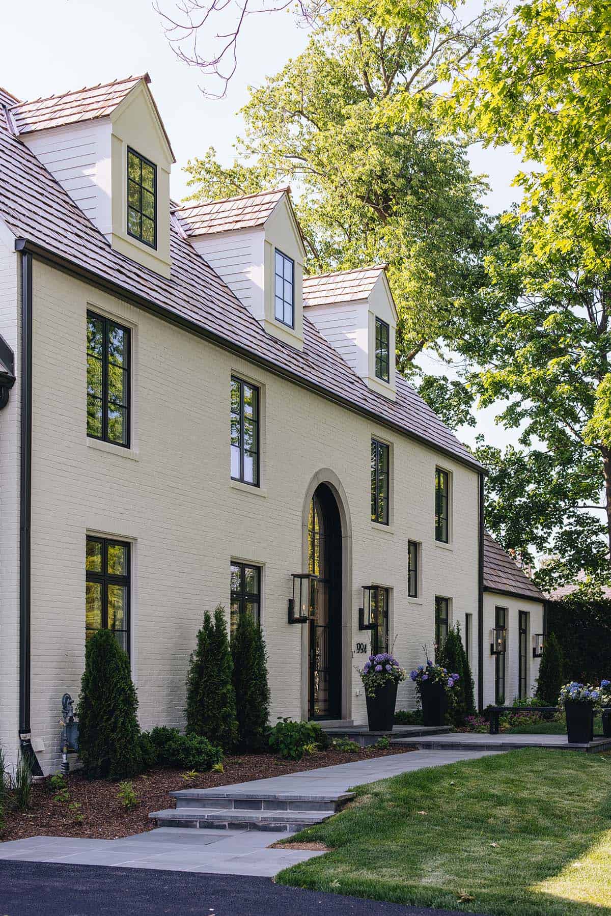 Front facade detail of cream brick manor with arched entry, dormers, and hydrangea planters