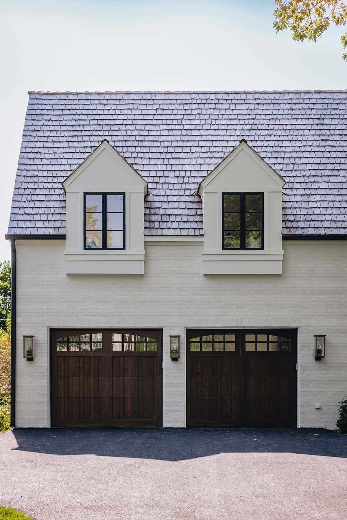 Garage facade with twin dormer windows, cedar shake roof, and dark wood carriage-style doors