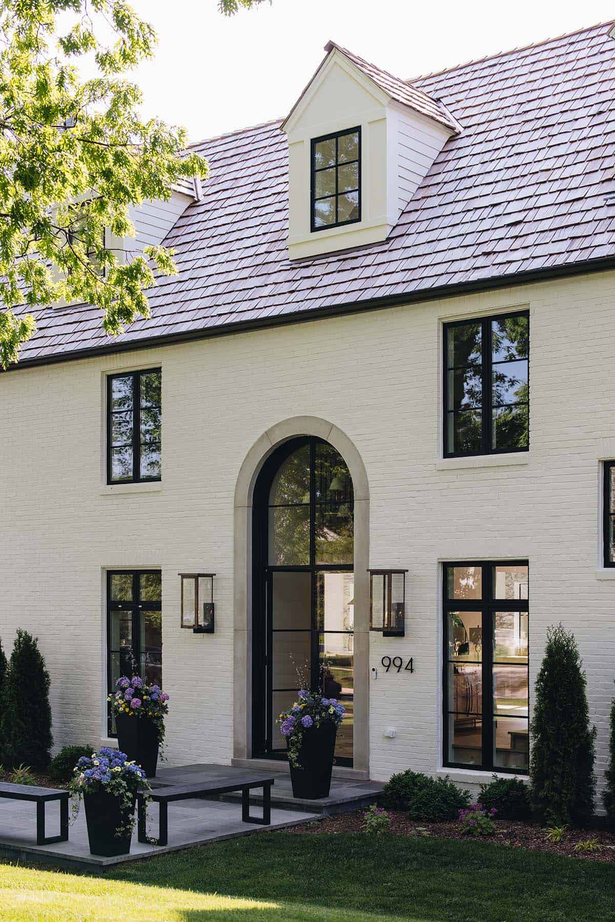 Front entry facade with arched glass door, black-framed windows, and dormer above at golden hour