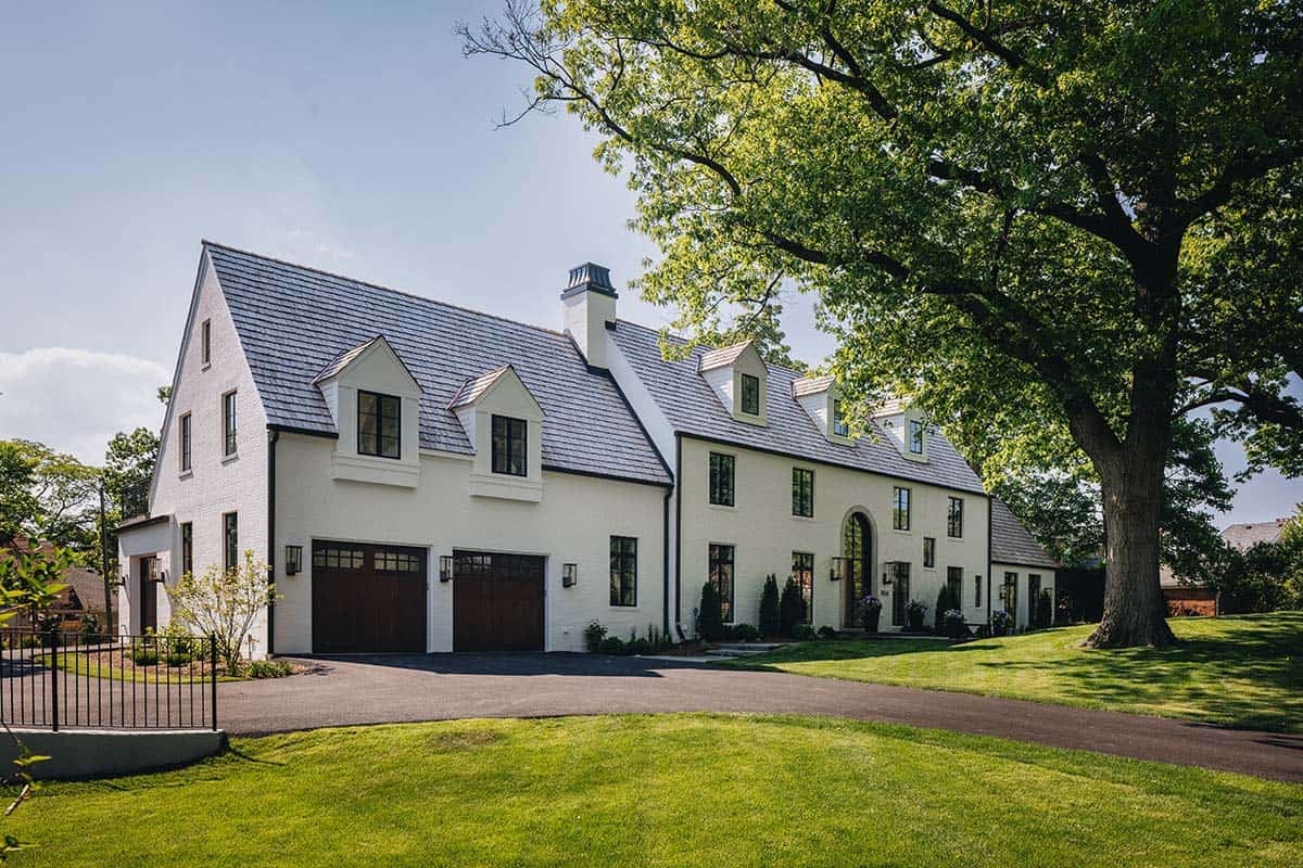 Beautiful white house with gabled roof, large trees, and manicured lawn.